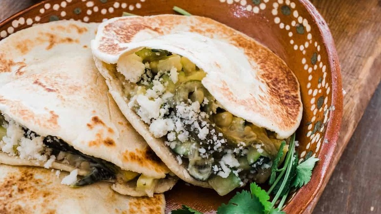 A brown painted bowl filled with gorditas stuffed with poblan chiles, cheese, onions