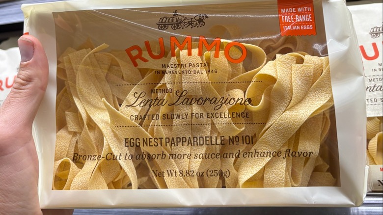 Hand holding a bag of yellow pasta with a rough texture