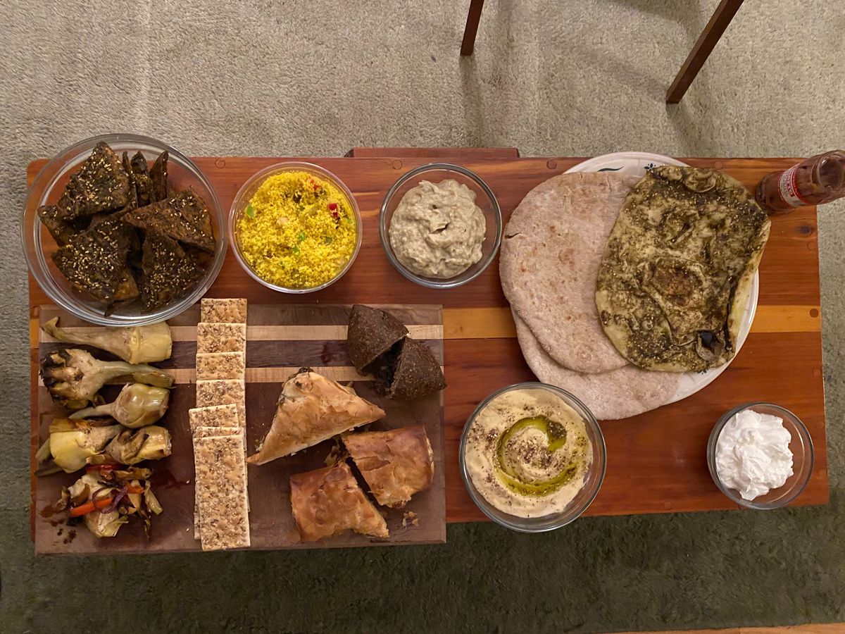 A spread of dips, chips, pita breads, filo pies, and grilled vegetables laid out on a wooden table