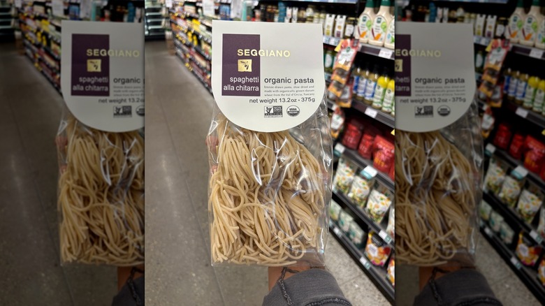 Hand holding a clear package of organic spaghetti pasta