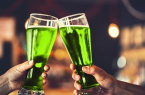 Two friends toast glasses filled with green beer.