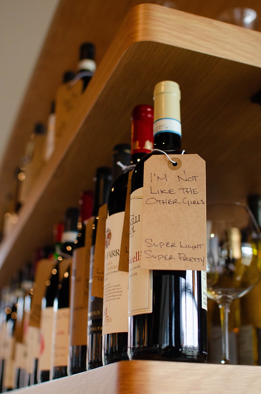 Bottles of wine sit on a shelf, with one in the foreground decorated with a label that says, "I'm not like the other girls. Super light, super pretty."