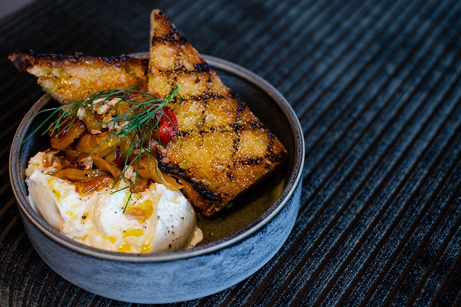 Grilled planks of bread, doused in olive oil, sit in a small plate with oil-drizzled burrata.