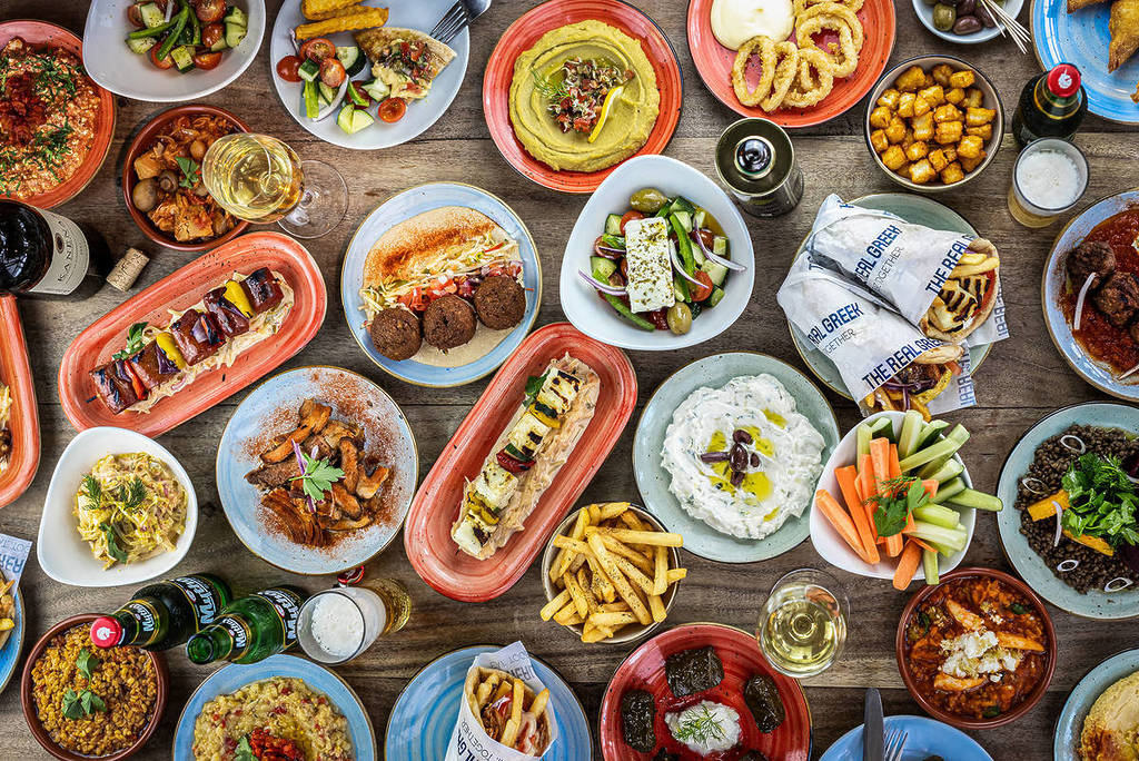 a birds-eye view of a table absolutely covered in Greek food, with over 20 dishes of food
