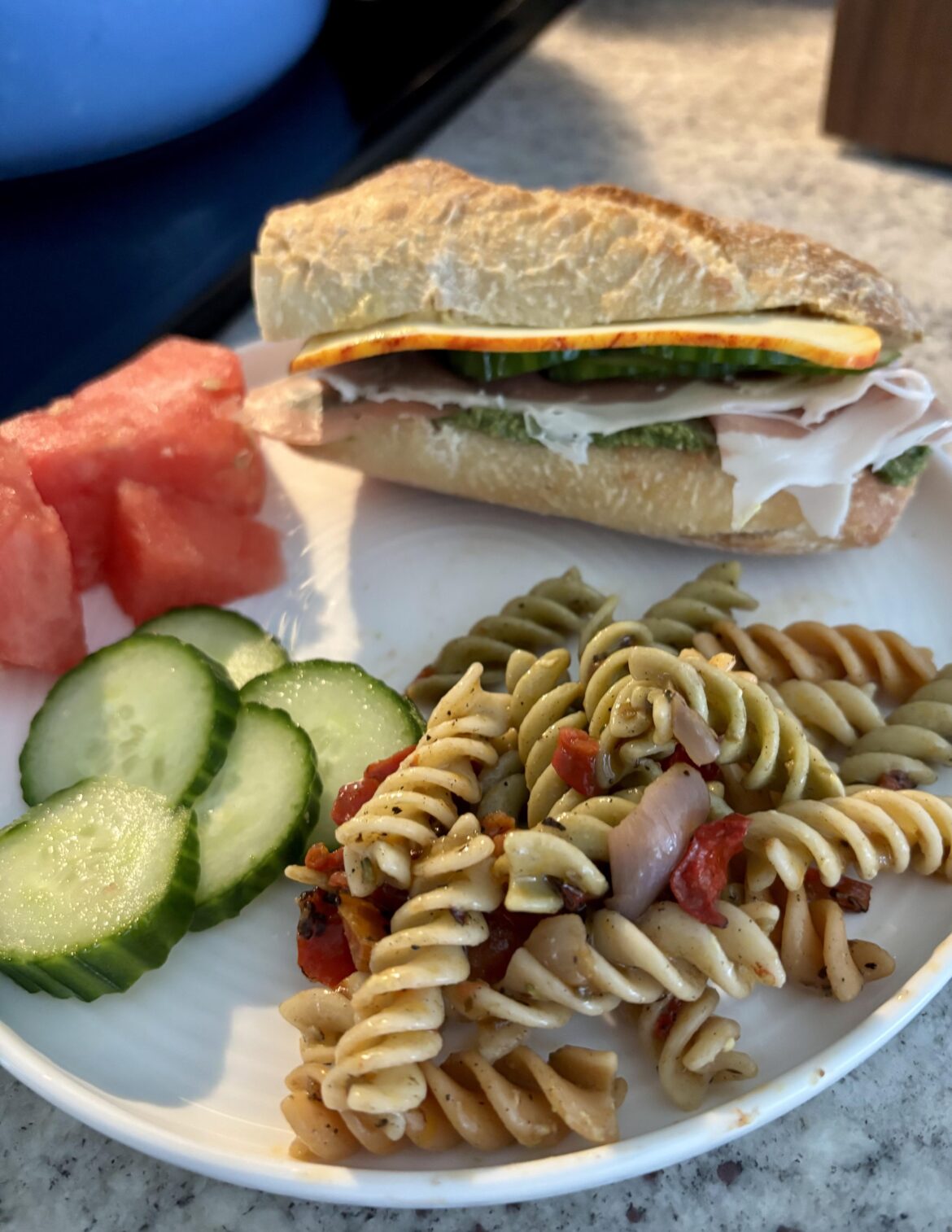 Prosciutto, cheese, homemade pesto, dijon mustard, cucumbers, tomatoes on baguette. Homemade pasta salad, watermelon, and more cucumbers for sides.