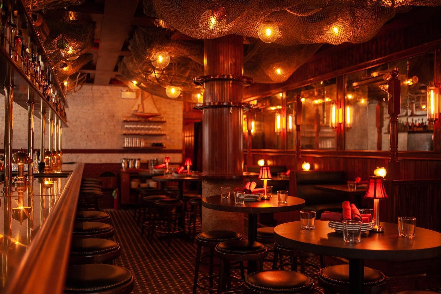three tables with tiny lamp dimly lit up next to a bar with stool and light fixtures hanging from the ceiling at Trivoli tavern