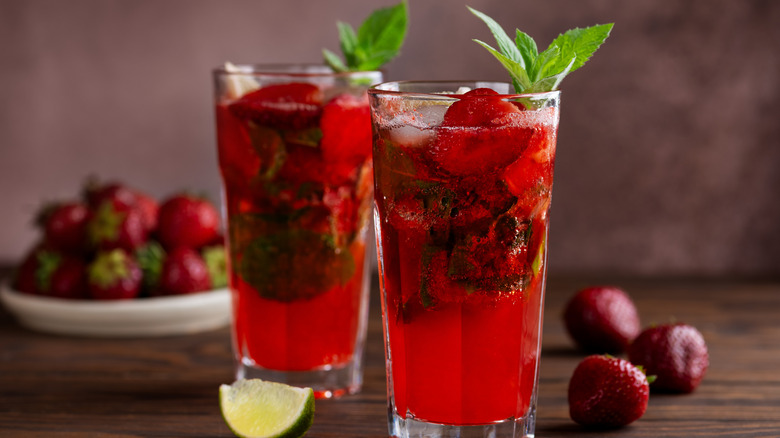 Red cocktail with dark ice cubes, strawberries, and mint