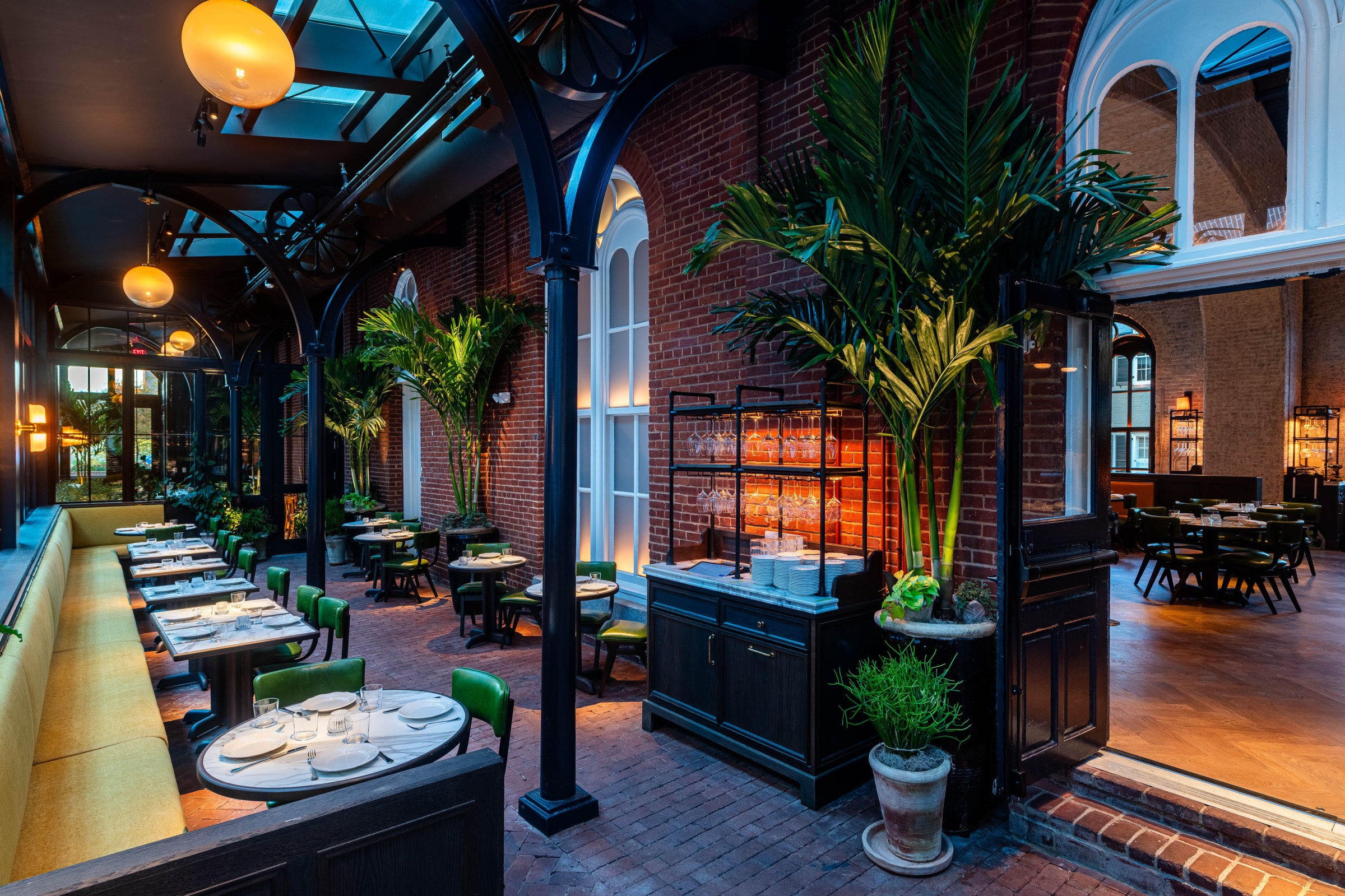 The glass-encased patio has warm mood lighting and brings nature indoors with verdant plants.