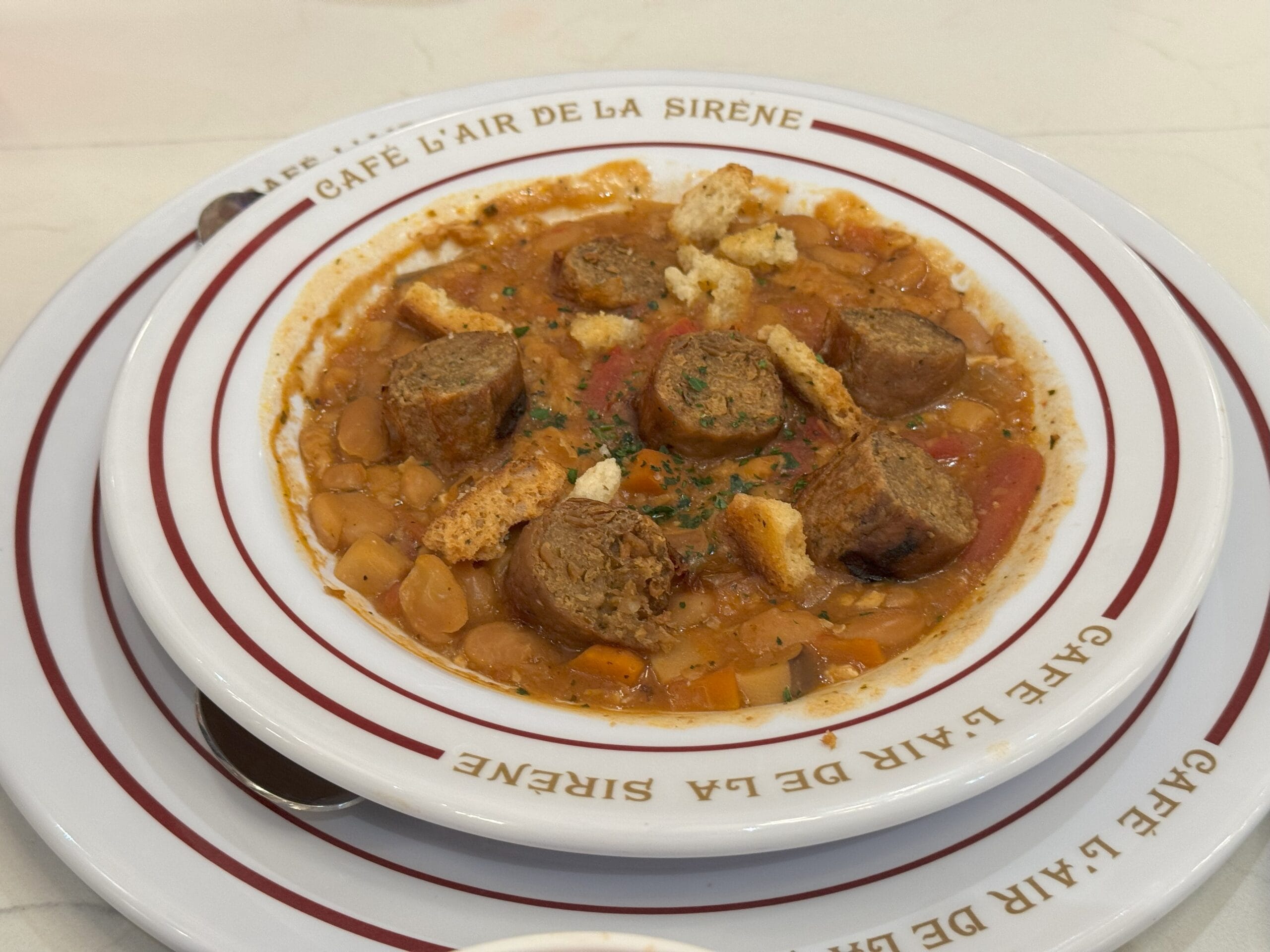 A hearty bean stew with sausage and croutons, served in a Café L’Air de la Sirène dish—perfect for your Epic Universe review.