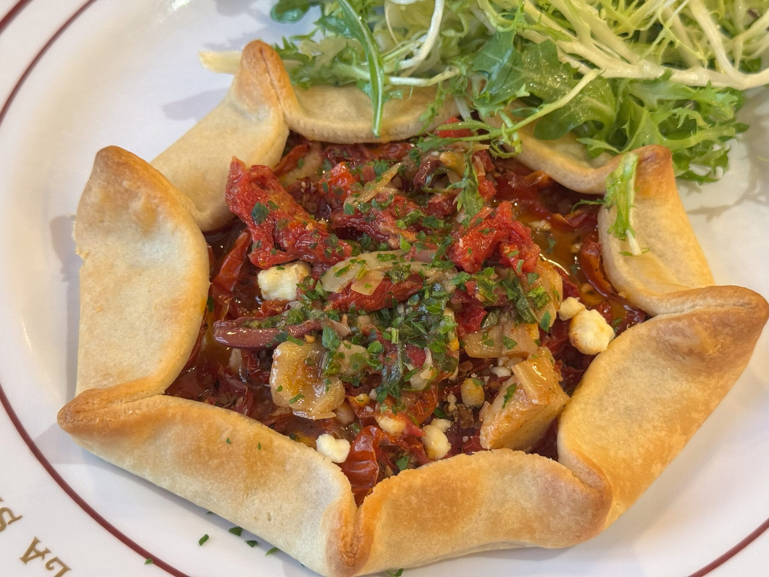 A savory tart with a folded crust, topped with veggies and herbs, served at Cafe L’air de la Sirène in Epic Universe.