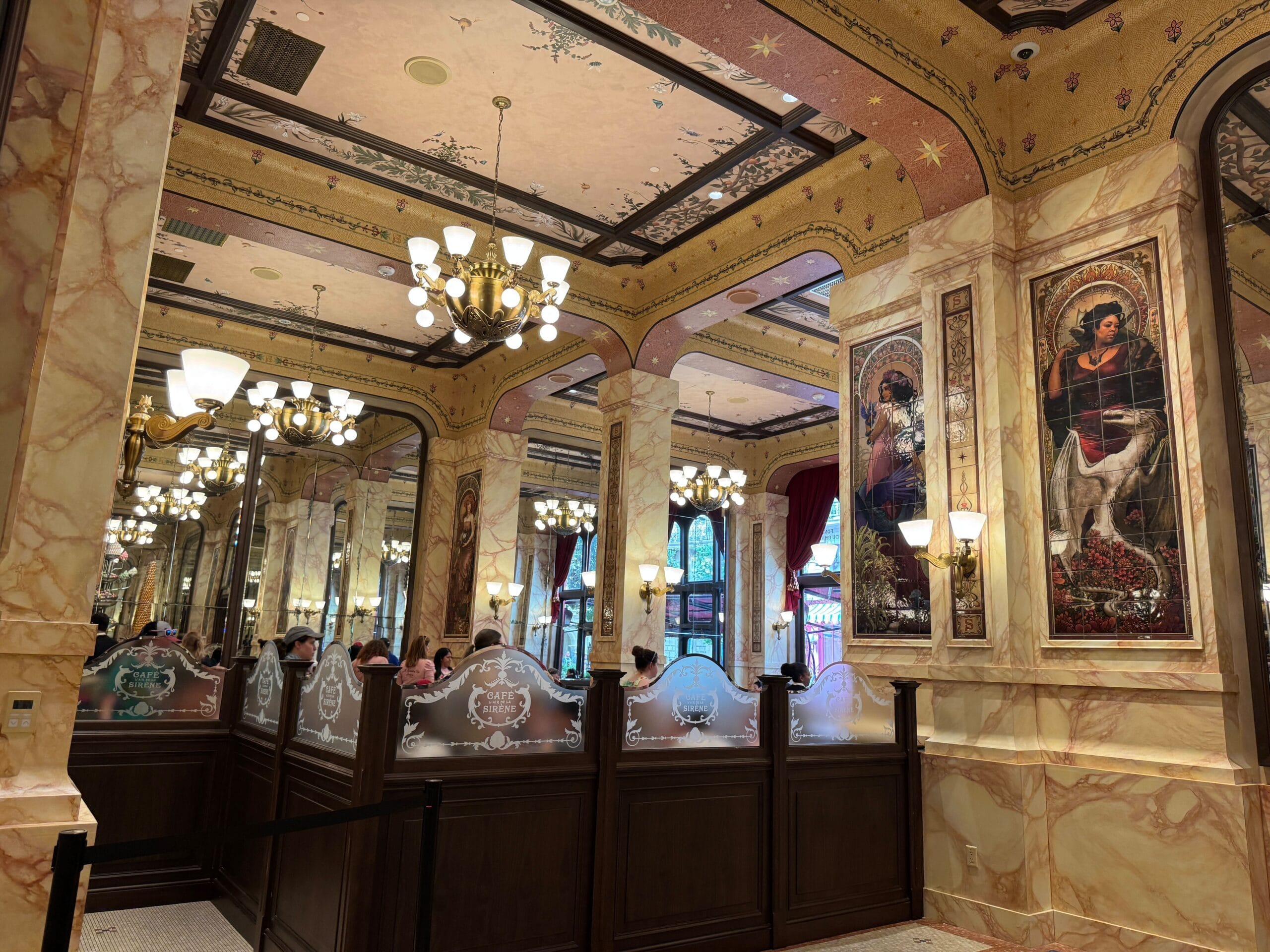 Cafe L’air de la Sirène features marble walls, chandeliers, grand mirrors, and elegant paintings of women on columns.