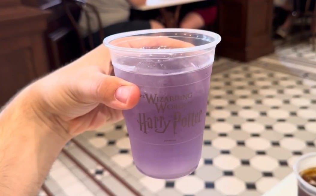 A hand holds a plastic cup of purple drink with a “Wizarding World of Harry Potter” logo at Epic Universe.