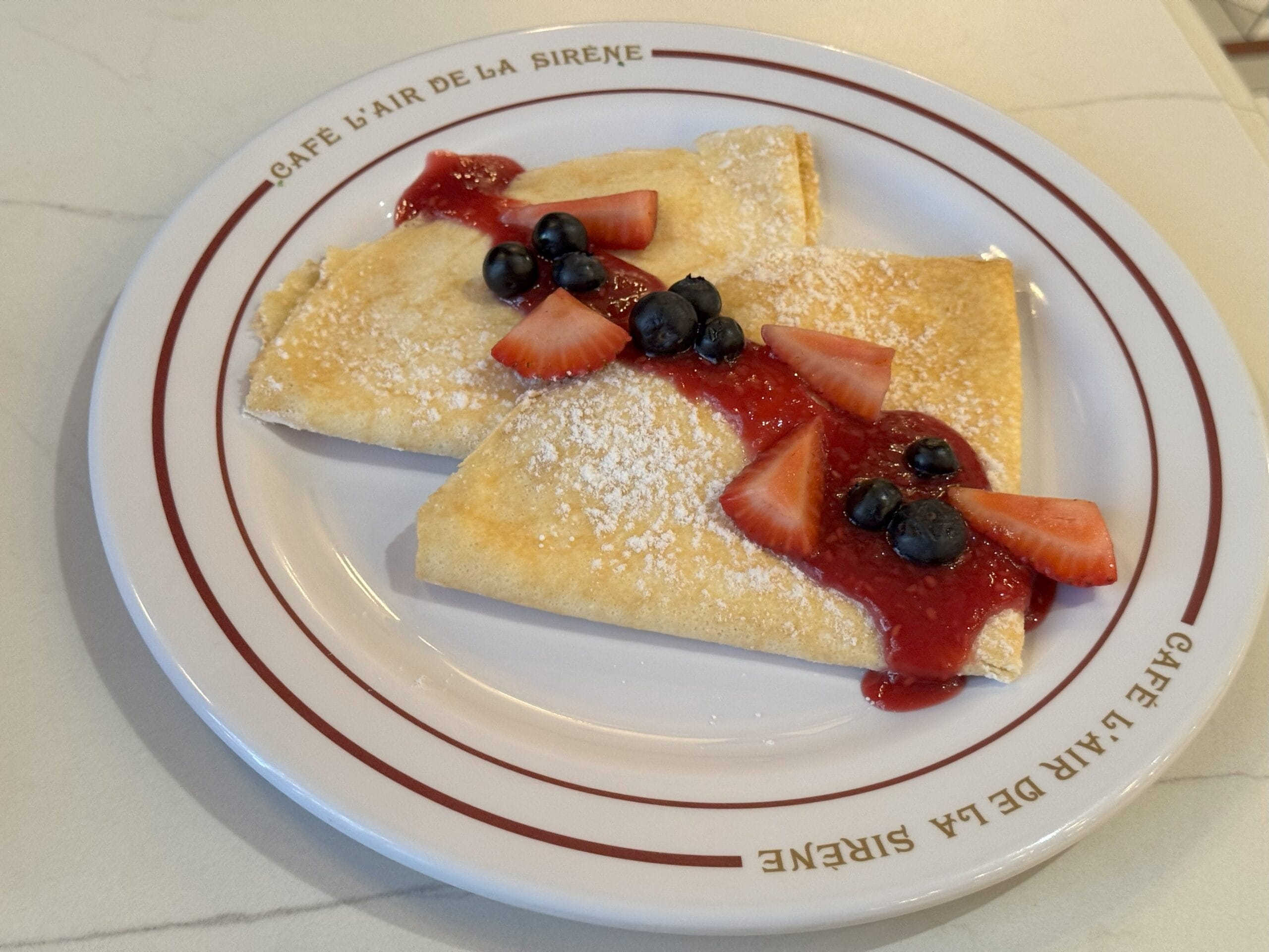 Two folded crepes at Cafe L’air de la Sirène, topped with strawberry sauce, berries, and sugar in Epic Universe.