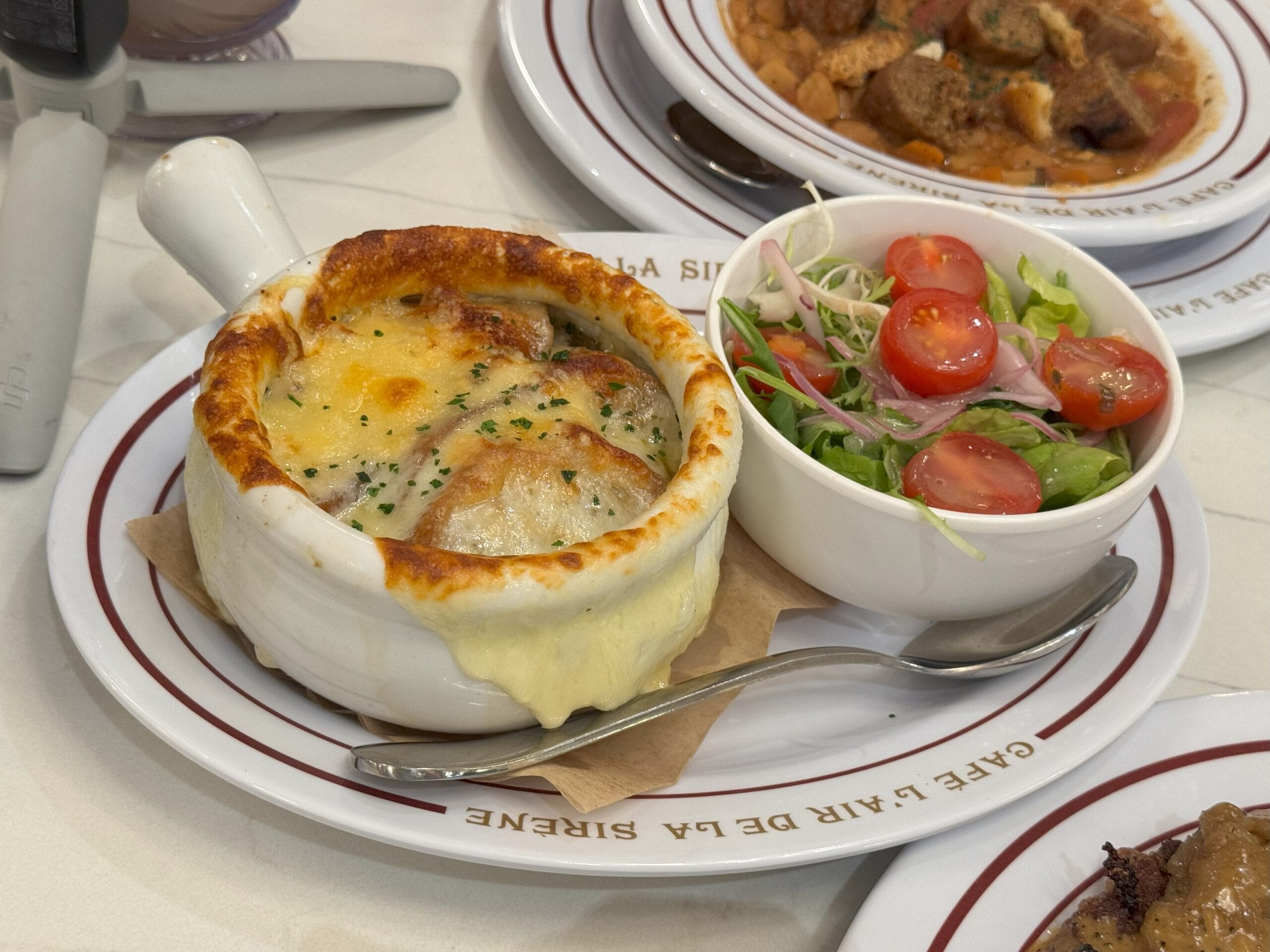 Baked French onion soup at Cafe L’air de la Sirène, near Epic Universe, served with a fresh salad of lettuce and cherry tomatoes.