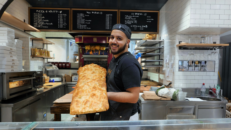 A chef holds up a full pizza bianca behind the counter at Rosioli