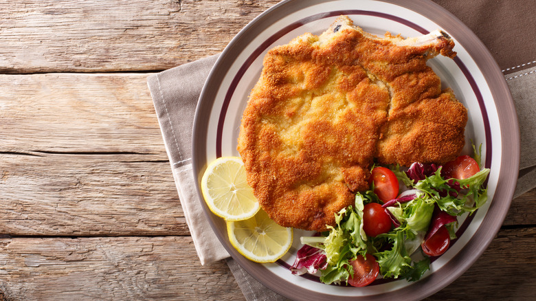 Fried veal chop on plate with salad and lemon slices