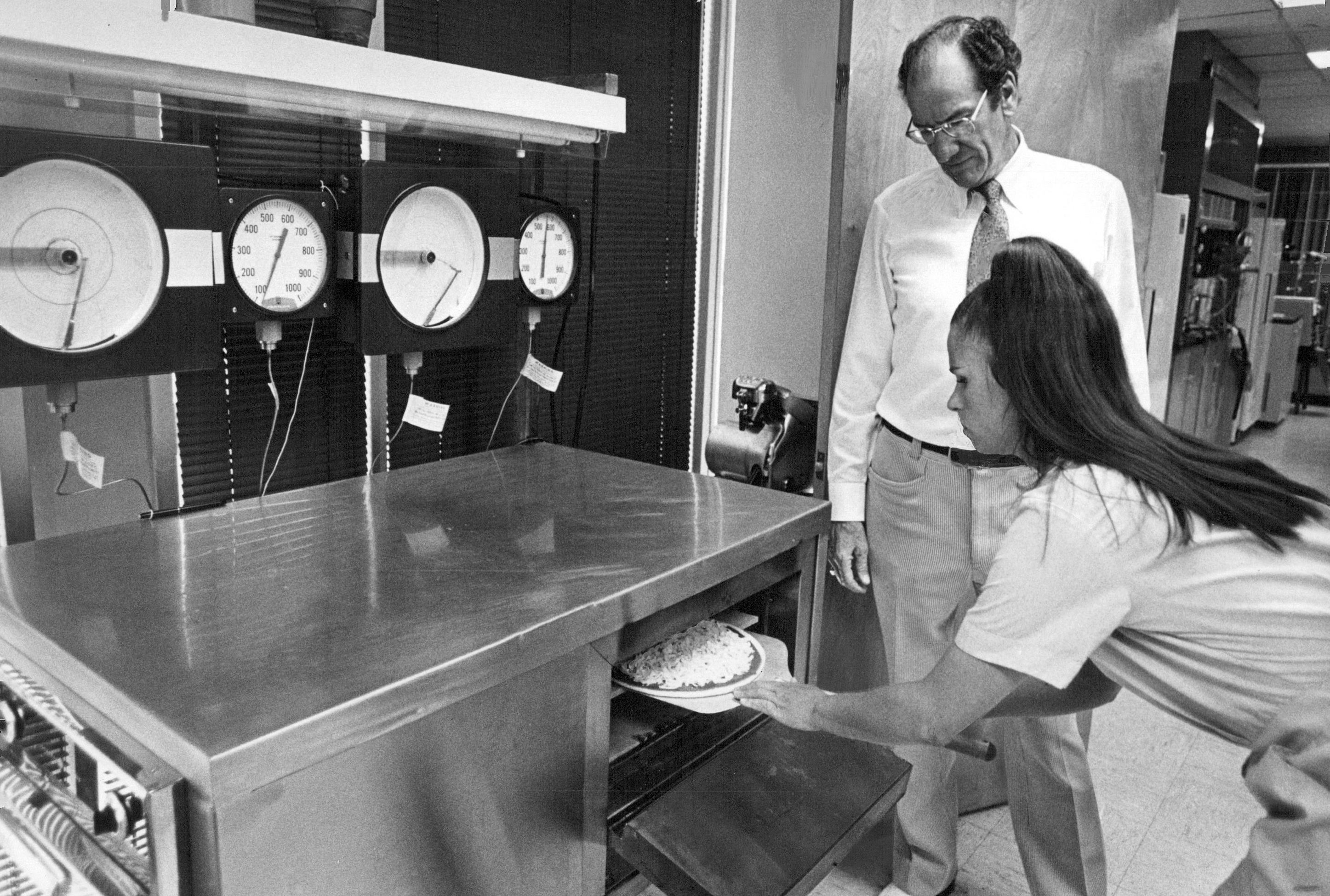 Black and white photo of Barbara Walters placing a pizza in an oven during a Leprino mozzarella cheese test.