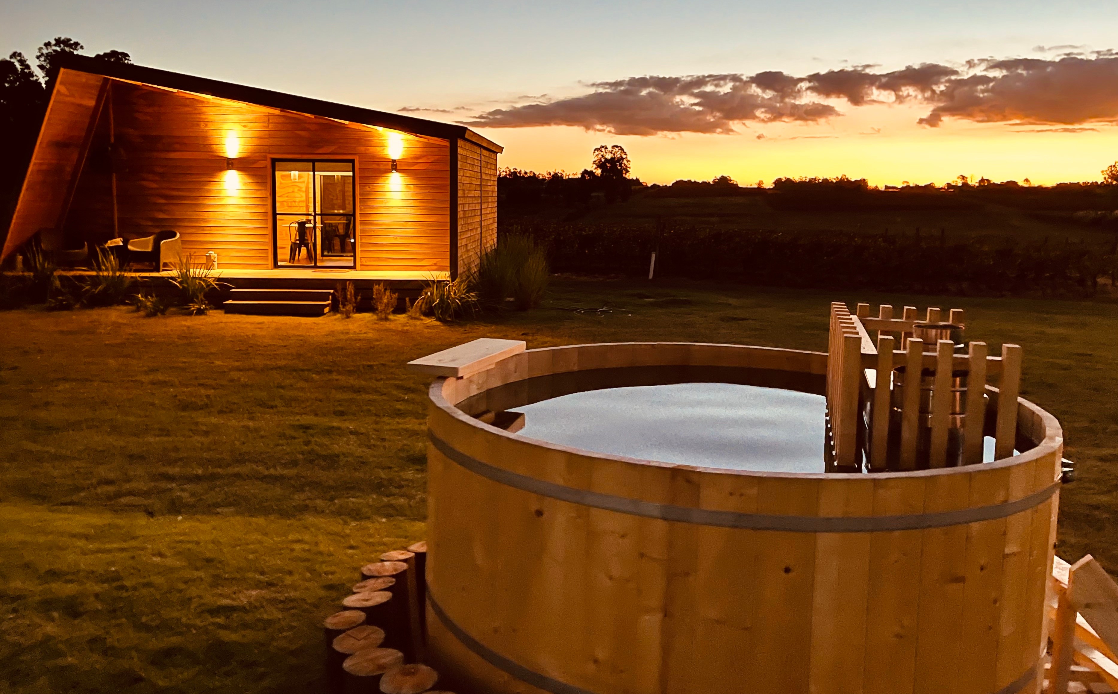 Wooden hot tub and illuminated cabin at sunset.