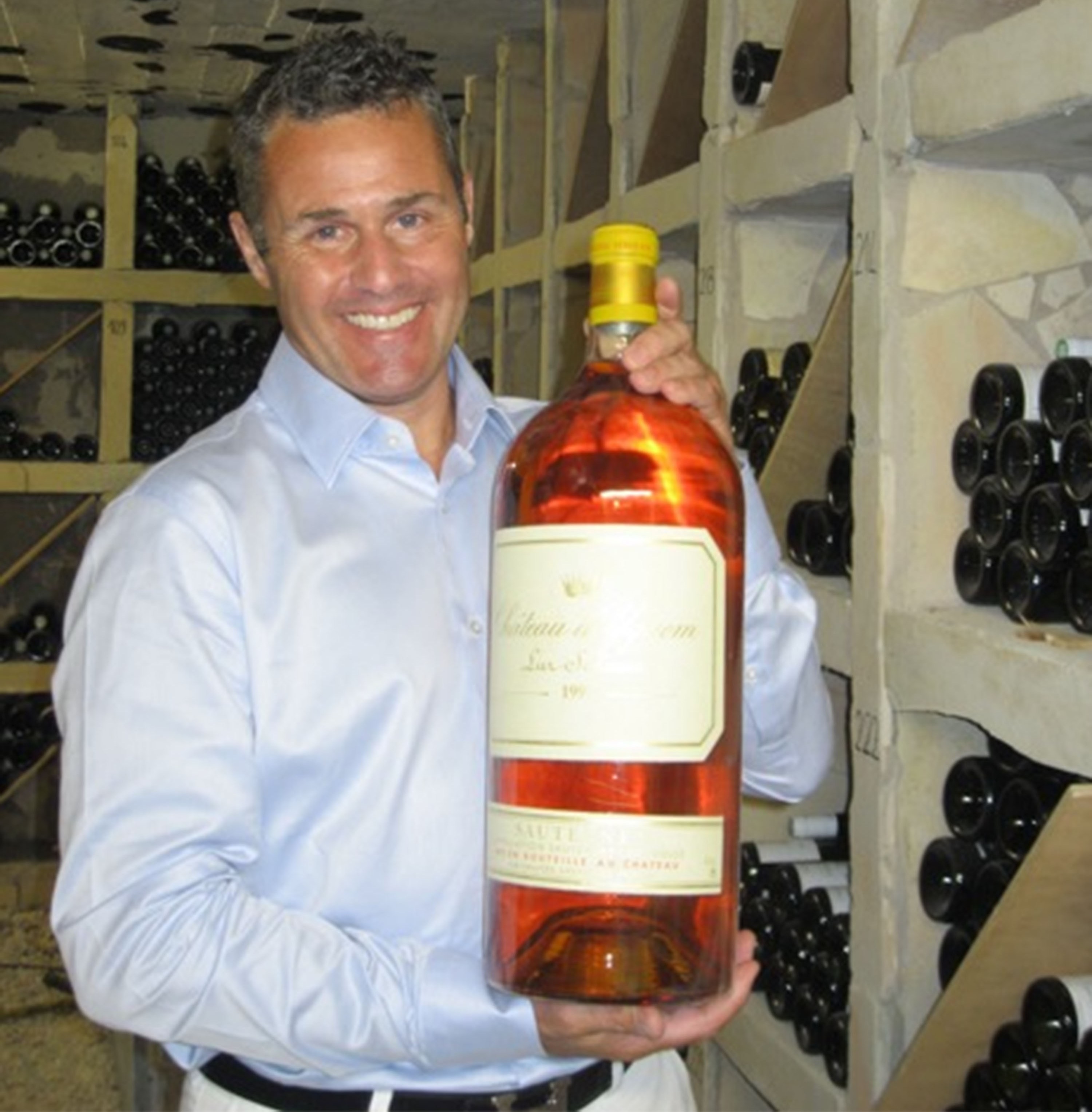 Stephen Burton holding a large bottle of wine in a wine cellar.