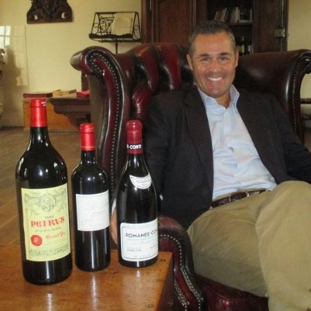 Man sitting in a chair with three bottles of wine.