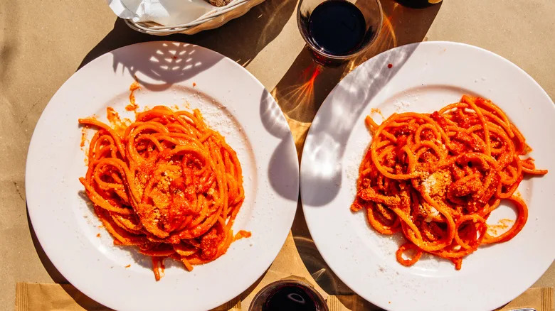 Top view of two white plates filled with spaghetti with pomodoro sauce and glasses of wine on the side