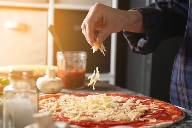 Woman sprinkles grated cheese onto homemade pizza base