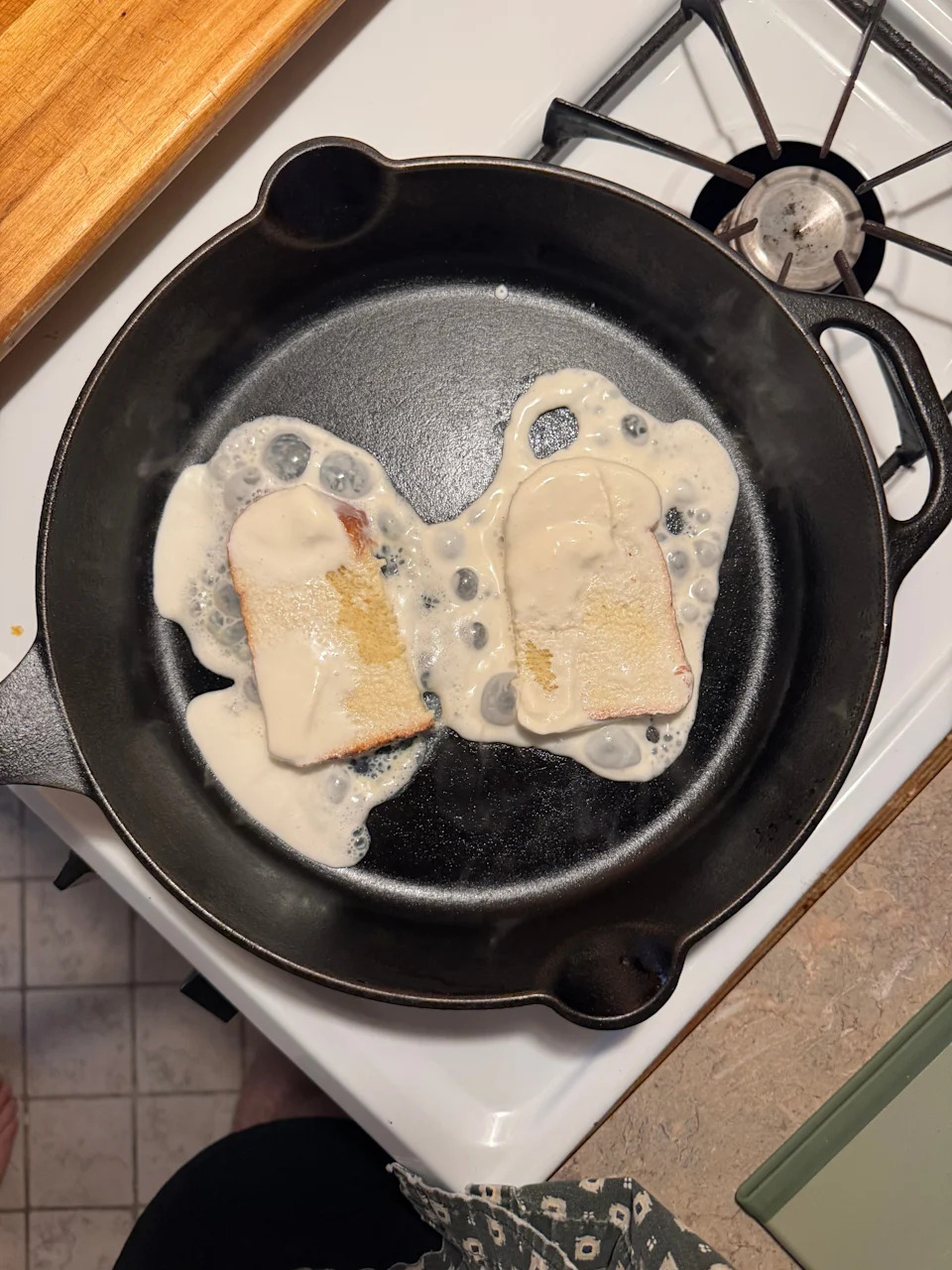 Two slices of bread frying in a skillet with batter, positioned on a stove