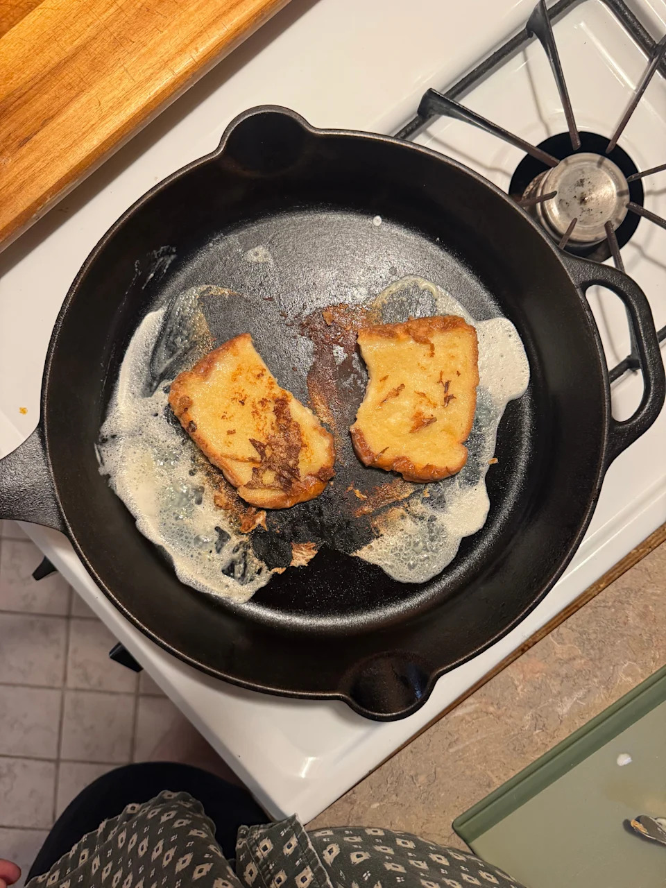 Two pieces of toast in a cast iron pan on a stove, slightly charred and surrounded by melting butter
