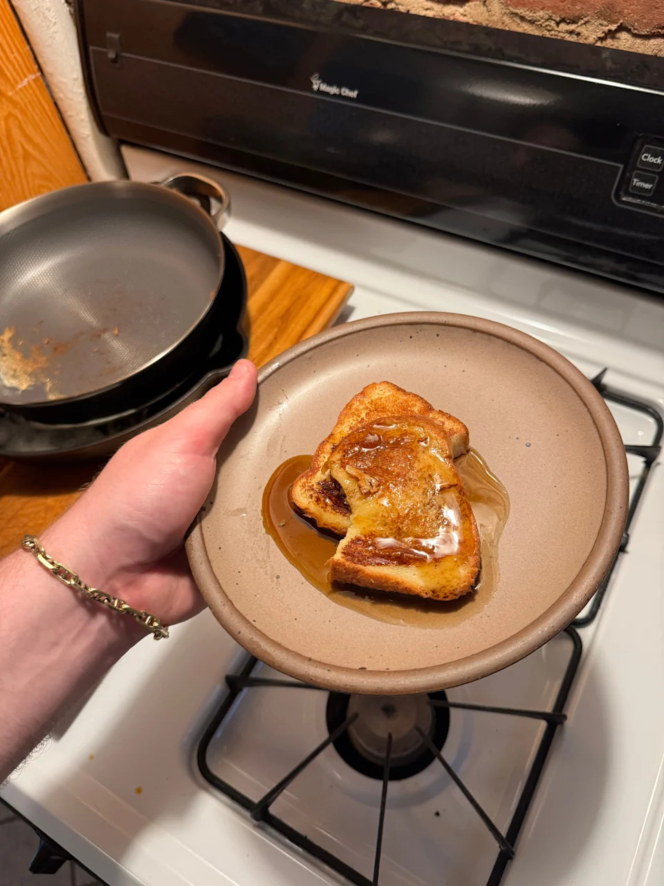 A plate with two slices of French toast topped with syrup, held over a stove with a pan in the background