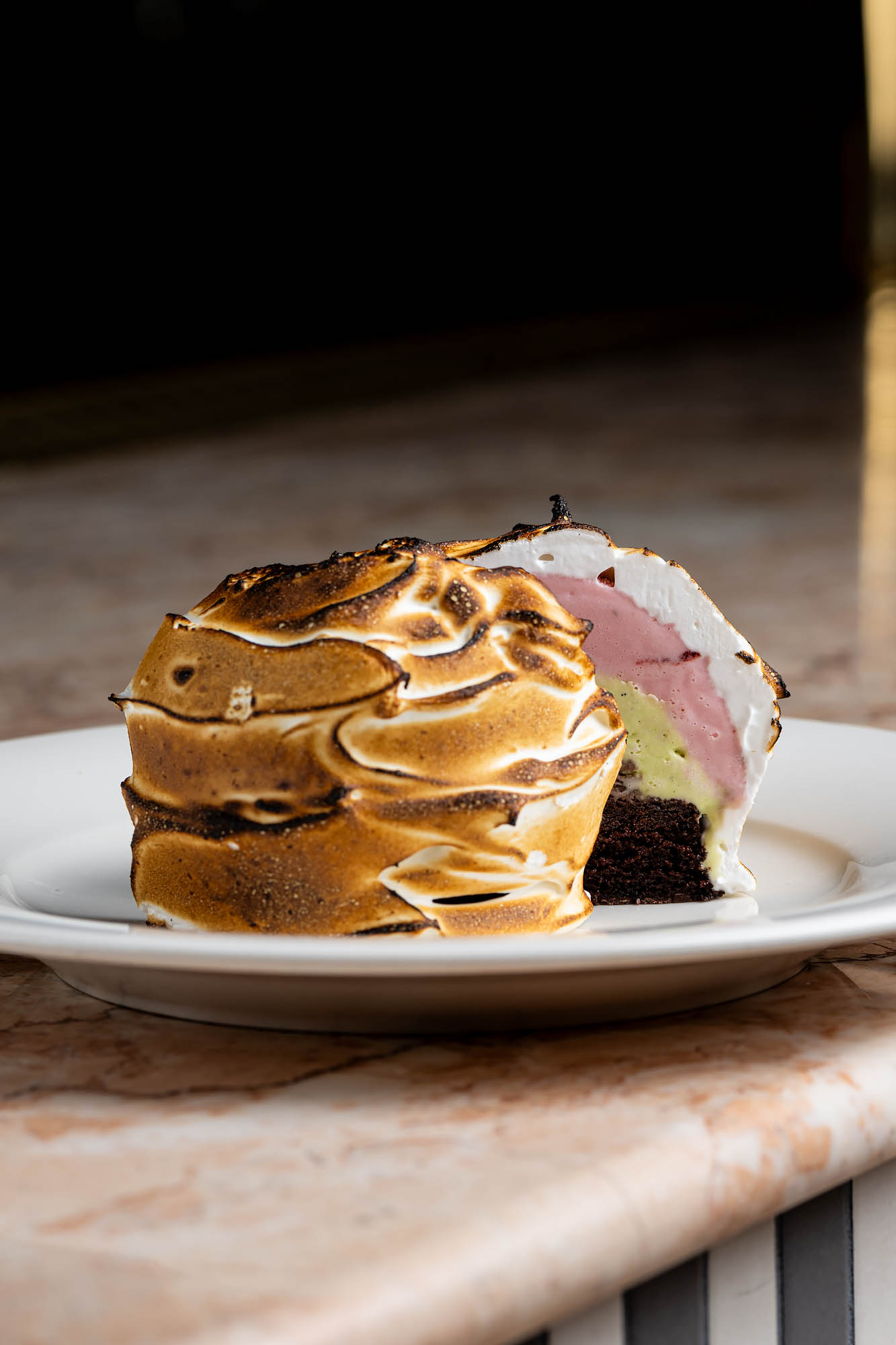 A white plate holding a spumoni baked Alaska cut in half to reveal pink, green, and brown ice creams at the Georgian Room.