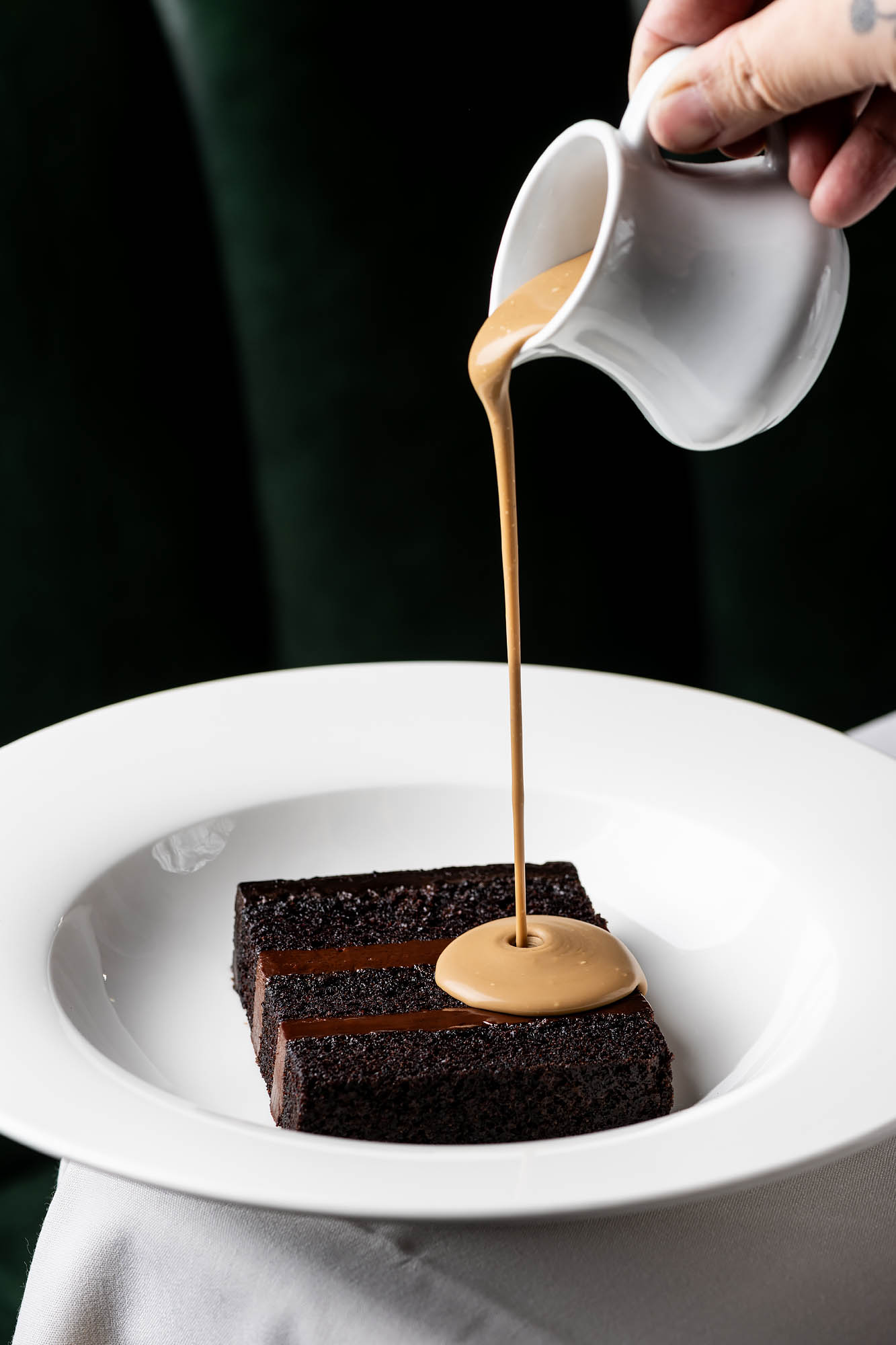 A white dish holding a slice of chocolate cake with a brown sauce poured from above at the Georgian hotel. 