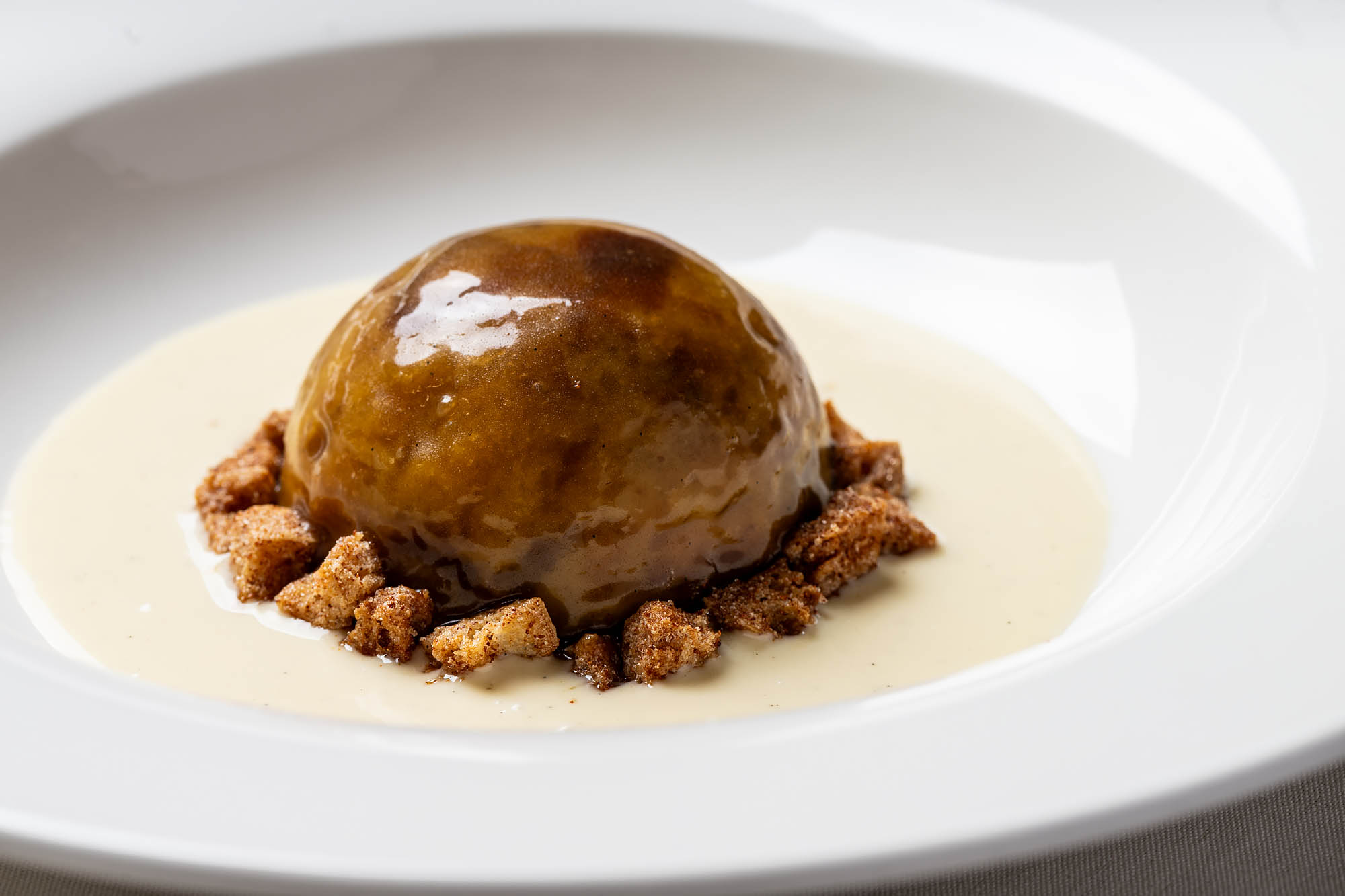 A white plate with a domed bread pudding accented with Cinnamon Toast Crunch cereal and sitting in a pool of white sauce at the Georgian.