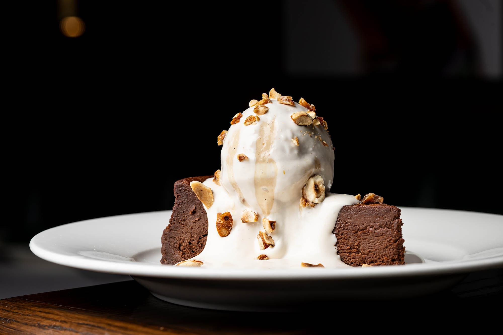 A white plate holding a wedge of flourless chocolate cake topped with a white cream and toasted hazelnuts at the Georgian Room. 