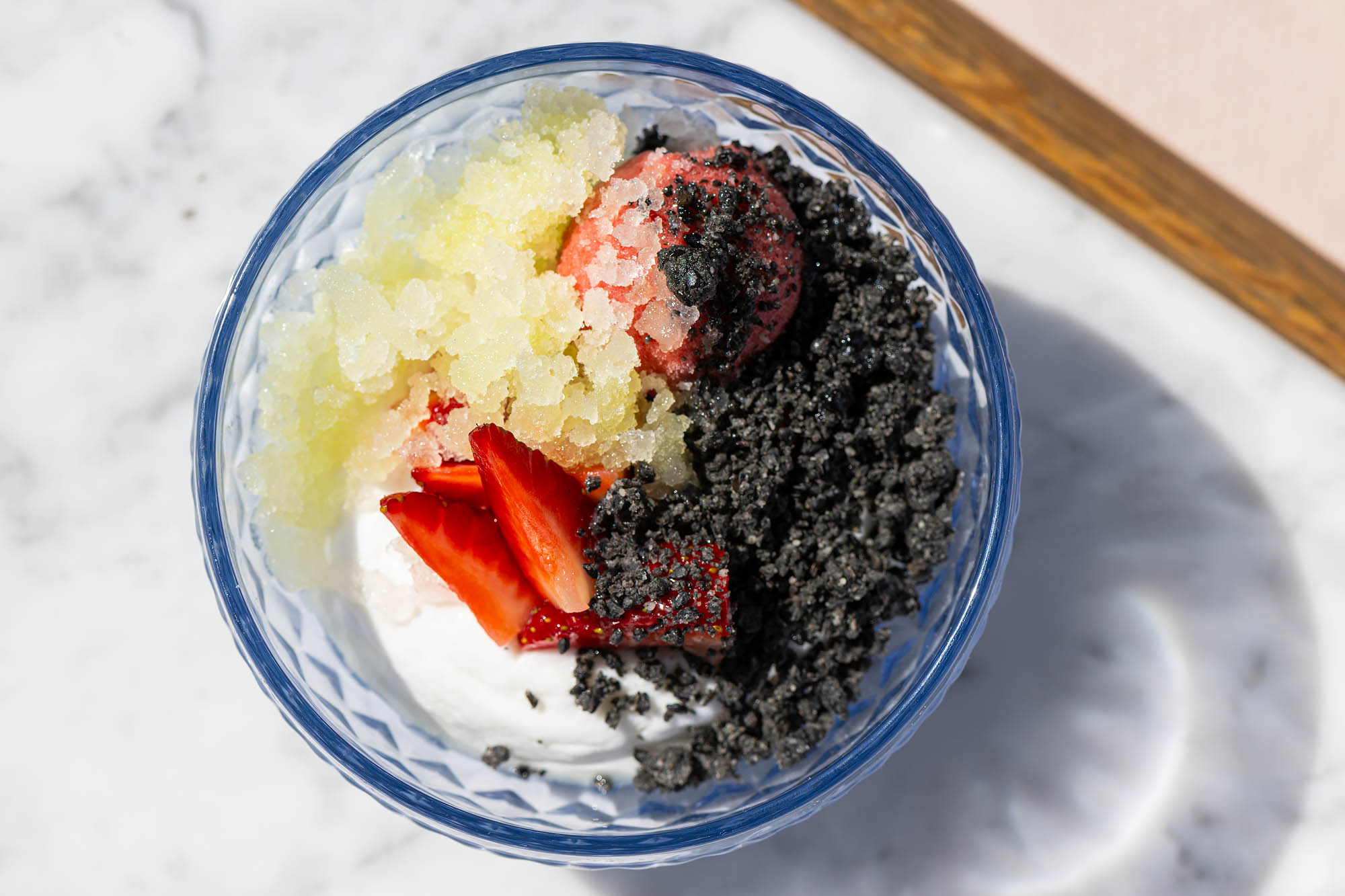 A blue glass bowl filled with coconut pudding and topped with black crumbles, macerated strawberries, and a pale green fennel granita at the Restaurant at the Georgian. 