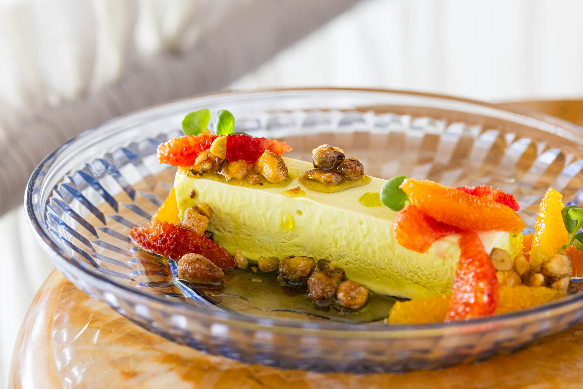 A glass plate holding a pale green rectangle of Pistachio Semifreddo topped with whole pistachios, micro greens, and segments of supremed citrus at the Georgian.