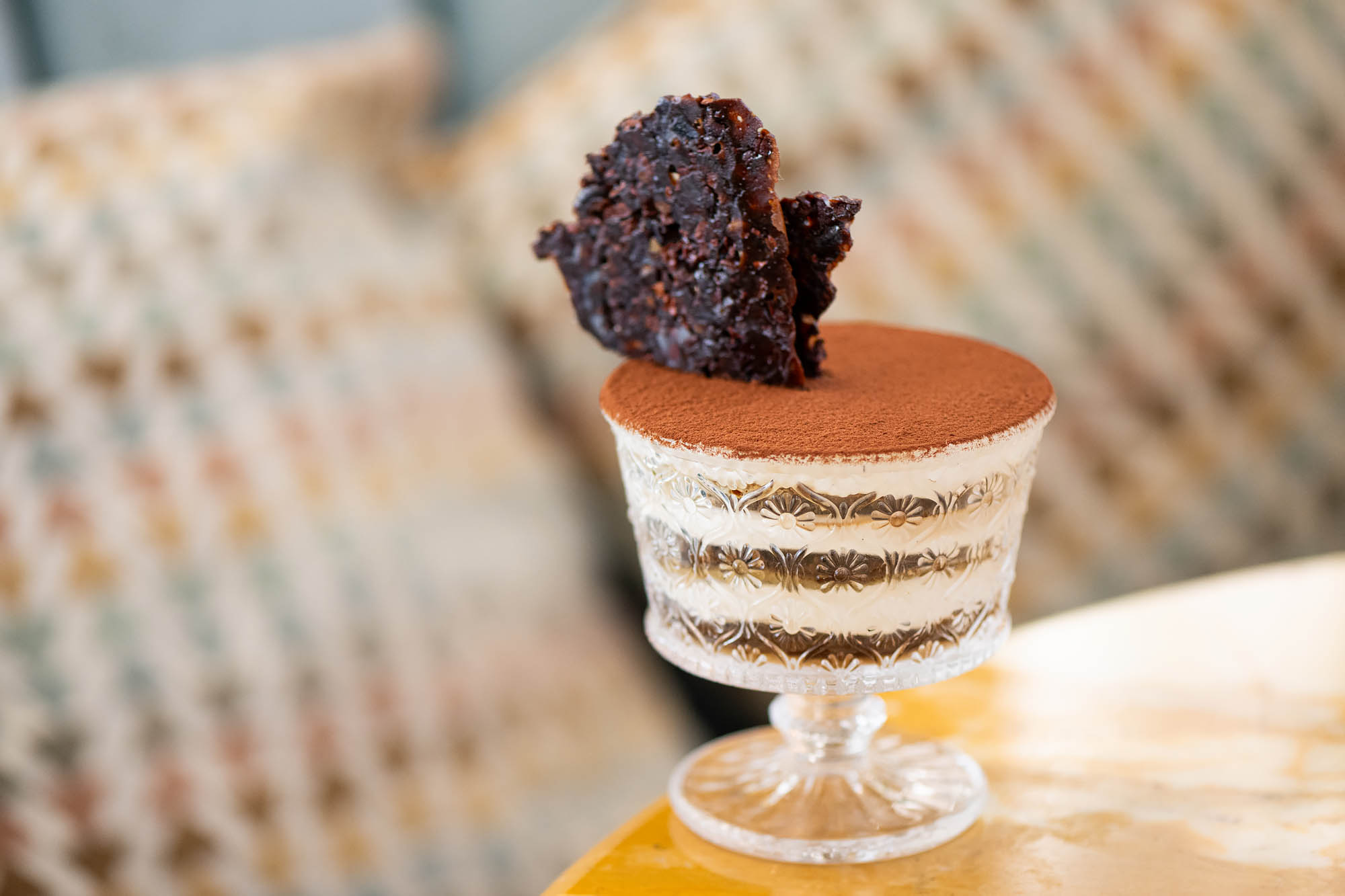 A tiramisu-filled glass goblet layered with lady fingers and cream and topped with cocoa powder and a dark brown brittle at the Georgian.