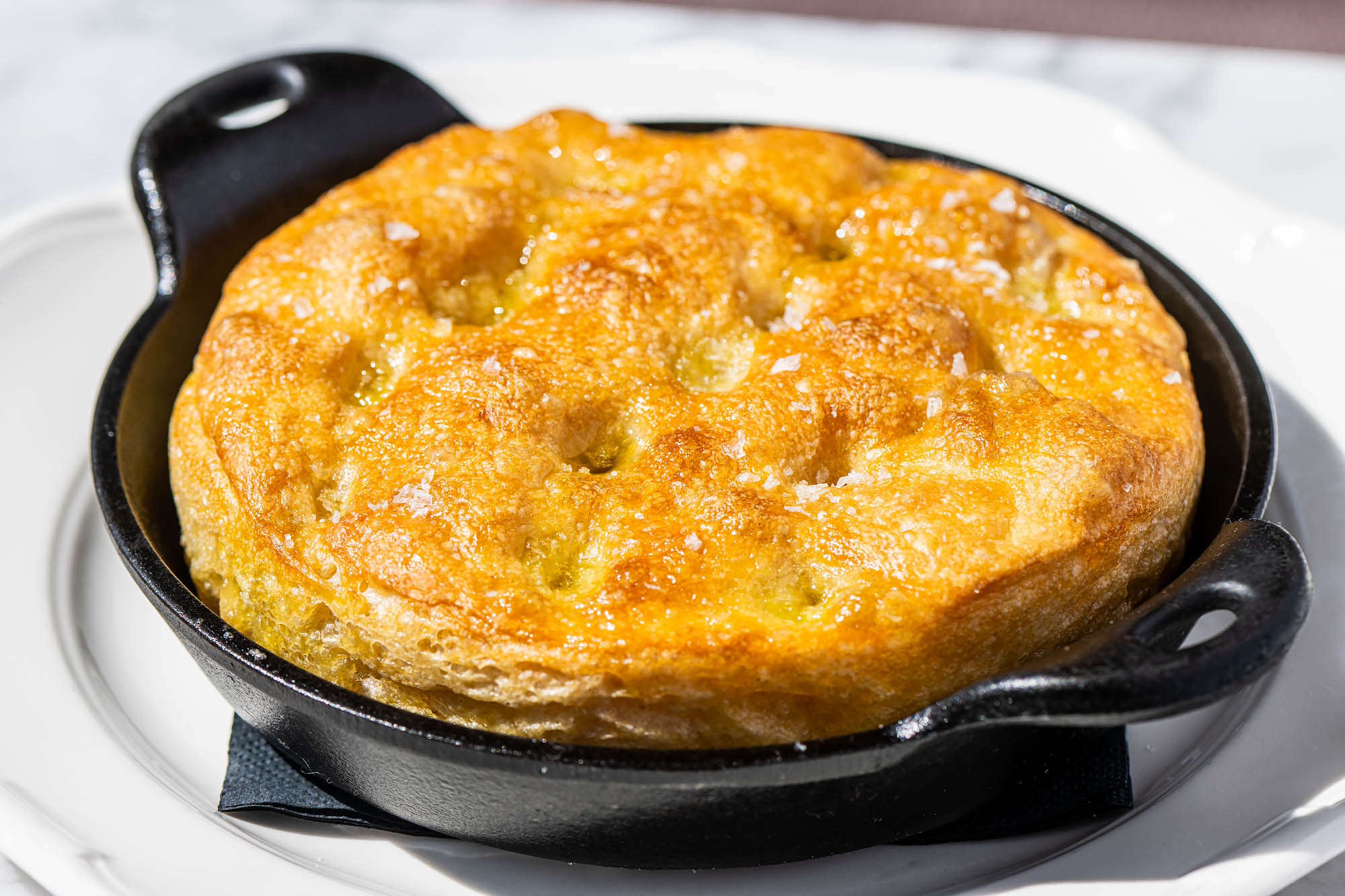 A cast iron dish holding golden focaccia  with dimples on its surface and plenty of flaky salt at the Georgian hotel.