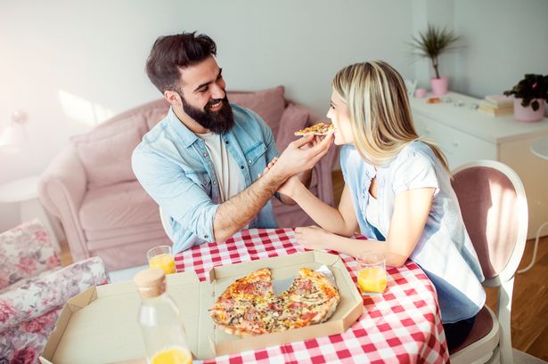 Smiling modern young man feeding his woman with pizza