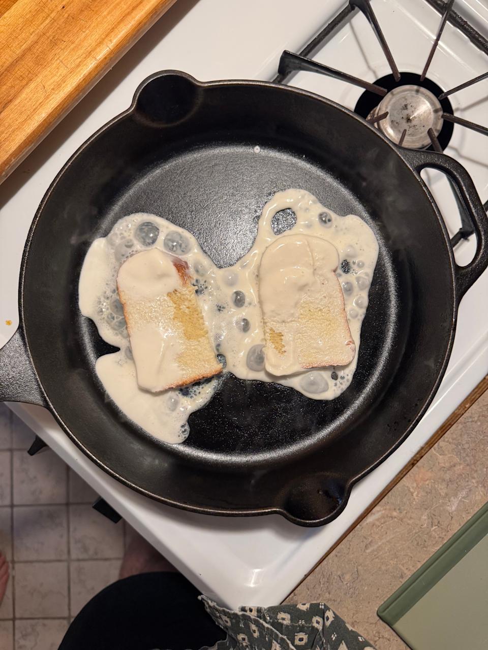Two slices of bread frying in a skillet with batter, positioned on a stove