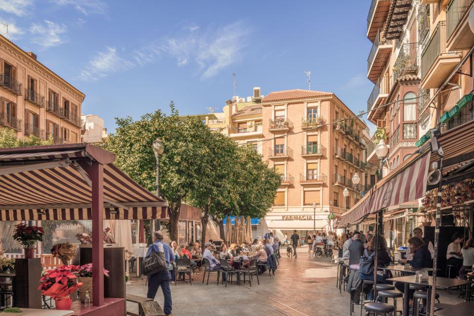 Plaza de las Flores in Murcia, Spain, with pedestrians and outdoor seating at restaurants.