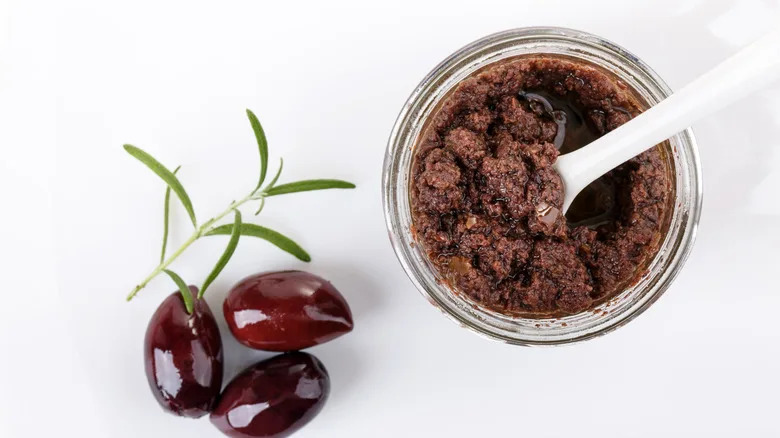Top view of an open jar of tapenade with some black olives on the side