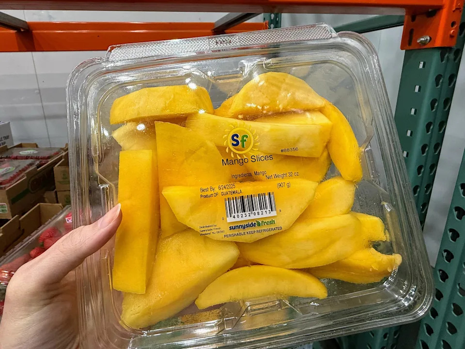 A hand holding a container of mango slices at Costco.