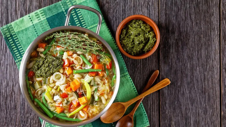 Pot of soup with pistou served on the side with a green kitchen towel on gray wood
