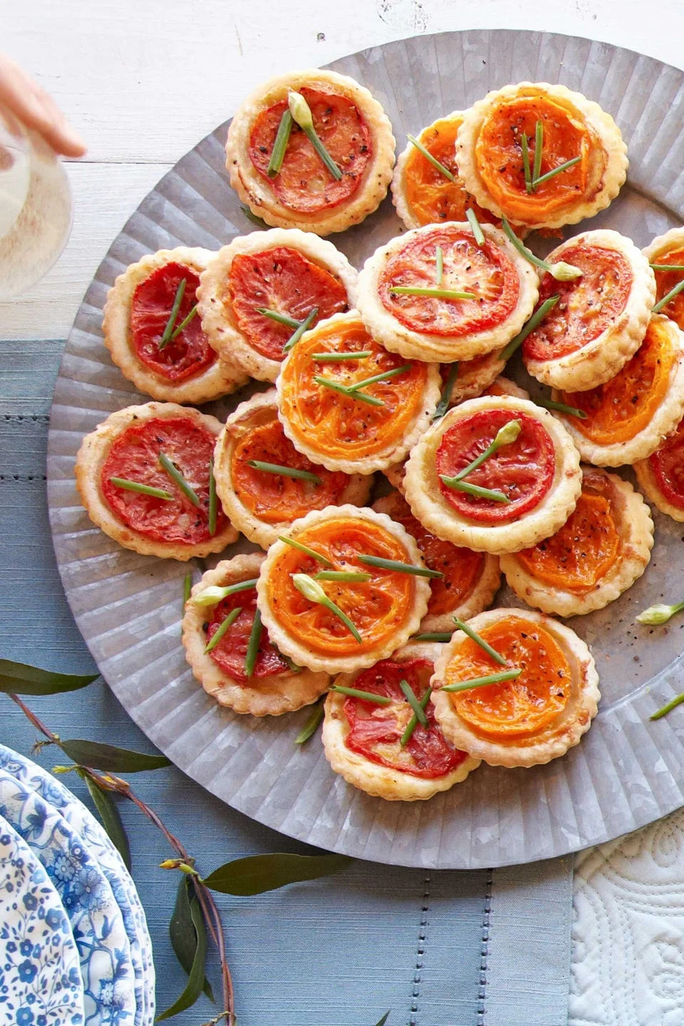 little tiny finger food tarts on a plate with small cherry tomato slices on top