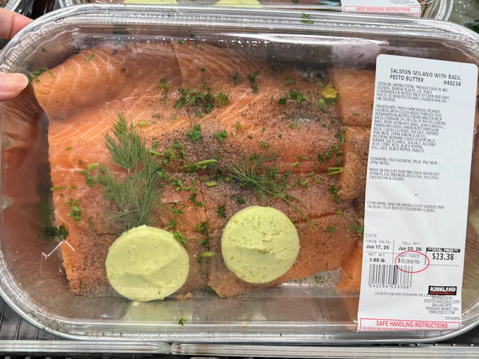 A hand holding a tin of salmon seasoned with butter and herbs at Costco.