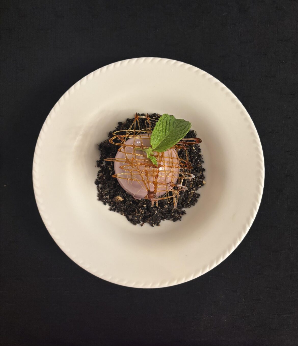 Dark chocolate shell filled with chocolate mousse and peach compote on a bed of chocolate almond crumble