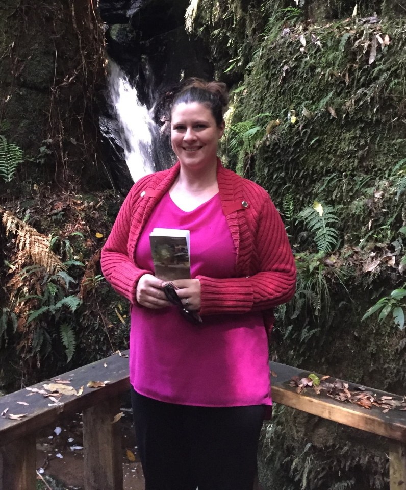 Woman standing in front of a waterfall in a rocky area.