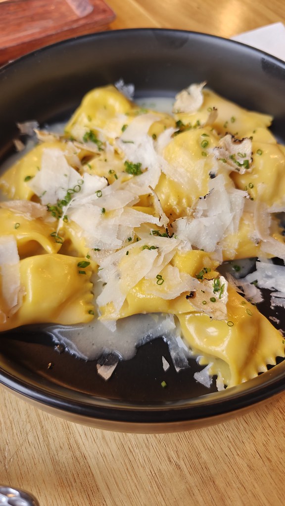 A black bowl containing about thirteen pieces of Agnolotti. Fresh parmesan is shaved on top.