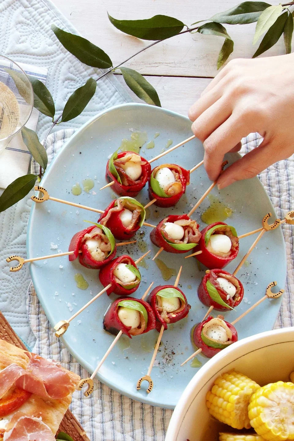 mozzarella, red pepper, and bacon skewers on a blue plate with a hand reaching in