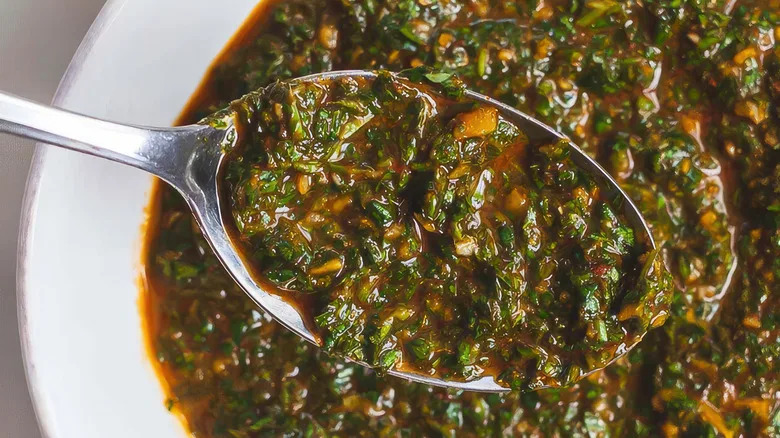 Closeup of a spoon filled with chermoula sauce with plate in the back